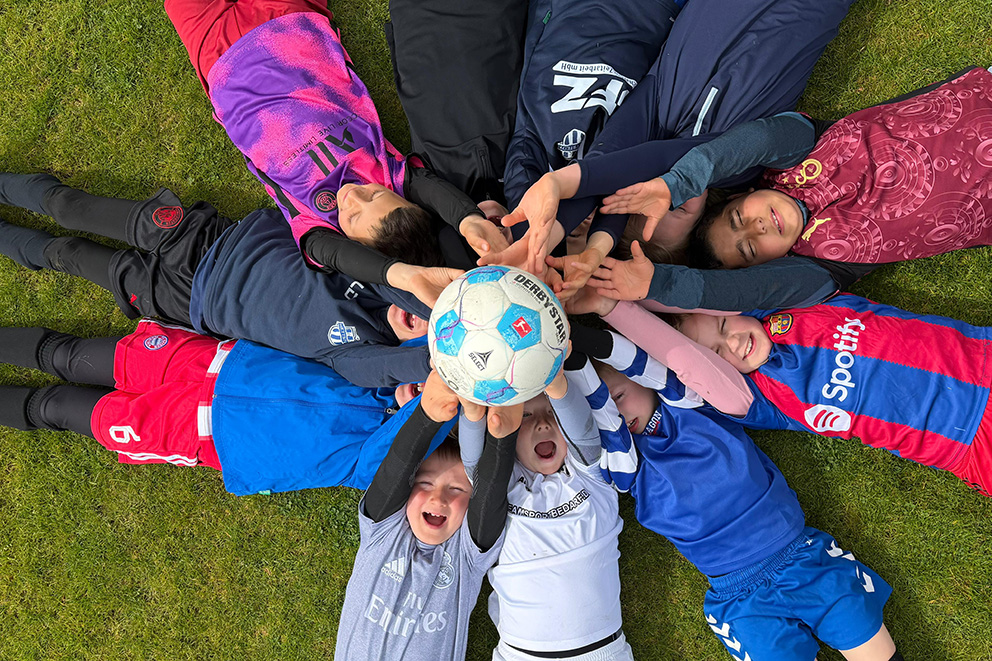 Junge Fußballspieler des FC Hettstedt halten gemeinsam einen Fußball in die Mitte