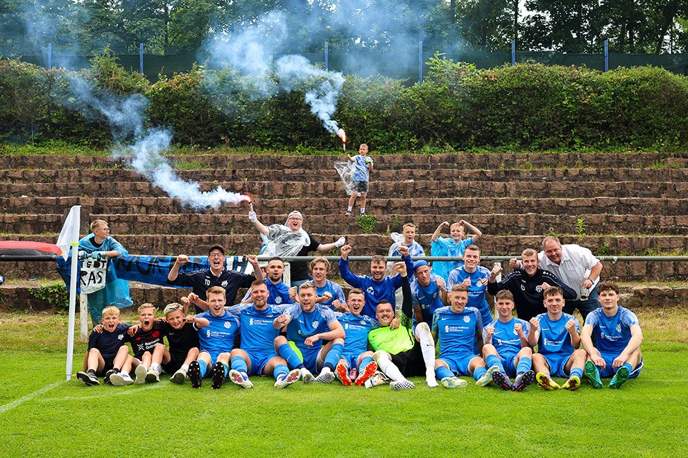 Jubelnde Mannschaft des FC Hettstedt mit Fans und Rauchfackeln am Spielfeldrand