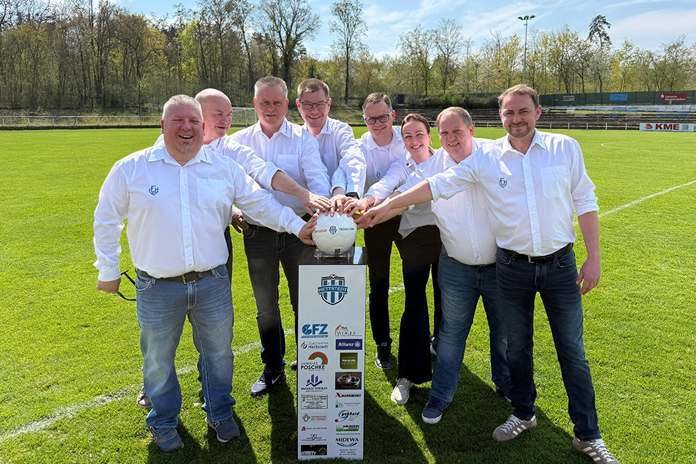 Vorstand des FC Hettstedt gemeinsam auf dem Fußballplatz mit Fußball und Sponsorentafel